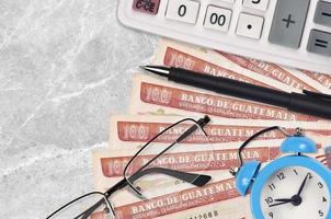 100 factures de quetzales guatémaltèques et calculatrice avec lunettes et stylo. prêt commercial ou concept de saison de paiement des impôts. le temps de payer les impôts photo