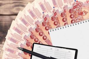 Éventail de factures de 100 bahts thaïlandais et bloc-notes avec carnet de contacts et stylo noir. concept de planification financière et de stratégie d'entreprise photo