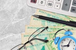 1 vrais billets brésiliens et calculatrice avec lunettes et stylo. prêt commercial ou concept de saison de paiement des impôts. le temps de payer les impôts photo