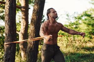 faire de l'exercice. bel homme torse nu avec un type de corps musclé est dans la forêt pendant la journée photo