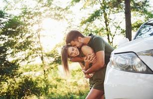 partie avant de la voiture blanche. beau jeune couple passe un bon moment dans la forêt pendant la journée photo