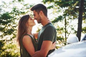 partie avant de la voiture blanche. beau jeune couple passe un bon moment dans la forêt pendant la journée photo