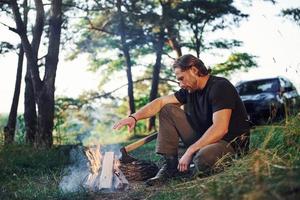 chauffage par le feu. homme en chemise noire près du feu de camp dans la forêt pendant son week-end photo