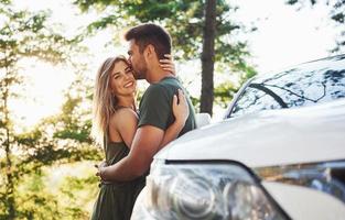 partie avant de la voiture blanche. beau jeune couple passe un bon moment dans la forêt pendant la journée photo