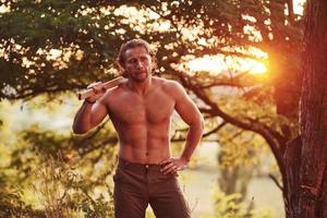 dans les bois. bel homme torse nu avec un type de corps musclé est dans la forêt pendant la journée photo