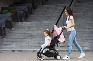 jolie jeune mère et sa petite fille en landau rose se promènent dans la ville photo