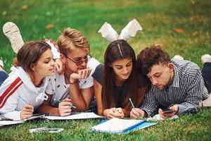 écrit sur papier. vue de face. groupe de jeunes étudiants en vêtements décontractés sur l'herbe verte pendant la journée photo