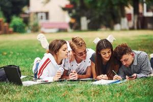 écrit sur papier. vue de face. groupe de jeunes étudiants en vêtements décontractés sur l'herbe verte pendant la journée photo