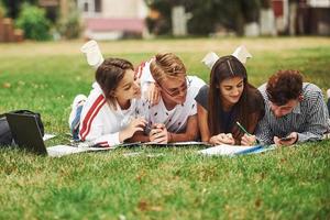 écrit sur papier. vue de face. groupe de jeunes étudiants en vêtements décontractés sur l'herbe verte pendant la journée photo