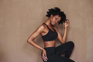 en tenue de sport noire. jeune belle femme afro-américaine en studio sur fond marron photo