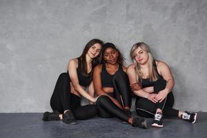 tout le monde a l'air satisfait. groupe de femmes multiethniques assises dans le studio sur fond gris photo