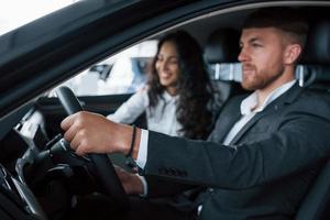 humeur joyeuse. beau couple réussi essayant une nouvelle voiture dans le salon de l'automobile photo