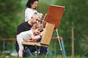 est-ce que je fais ça bien. grand-mère et grand-père s'amusent dehors avec sa petite-fille. conception de la peinture photo