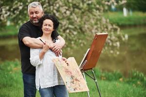 regardant dans la caméra. un couple d'âge mûr a des journées de loisirs et travaille ensemble sur la peinture dans le parc photo