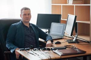 assis sur la chaise noire. l'examinateur polygraphique travaille au bureau avec l'équipement de son détecteur de mensonges photo