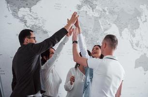 célébrer le succès. équipe de pigistes debout contre un mur avec une carte du monde dessus photo