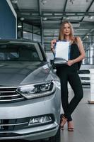 femme à la mode. fille et voiture moderne dans le salon. le jour à l'intérieur. achat d'un véhicule neuf photo