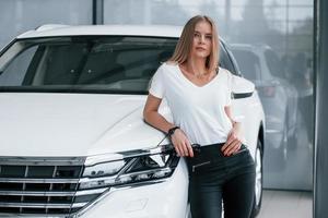 s'appuyant sur l'auto. fille et voiture moderne dans le salon. le jour à l'intérieur. achat d'un véhicule neuf photo