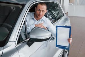 document montrant. directeur assis dans une voiture blanche moderne avec du papier dans les mains photo