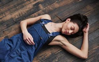 les yeux fermés. fille en uniforme bleu pour le travail est allongée sur un plancher en bois se détendre photo