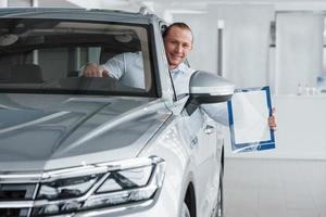 Bienvenue dans notre magasin. gestionnaire assis dans une voiture blanche moderne avec du papier et des documents dans les mains photo