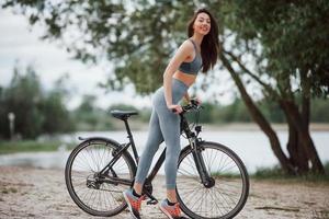 temps nuageux. cycliste féminine avec une bonne forme de corps debout avec son vélo sur la plage pendant la journée photo