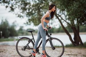 ce vélo est agréable. cycliste féminine avec une bonne forme de corps debout avec son véhicule sur la plage pendant la journée photo