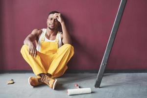 s'assoit et se repose. jeune travailleur afro-américain en uniforme jaune a du travail photo