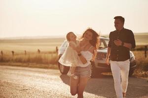 Dépêchez-vous. la famille passe du bon temps à la campagne près de l'automobile argentée au coucher du soleil photo