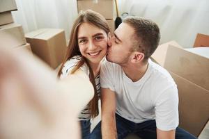 faire une photo. guy embrasse sa femme. joyeux jeune couple dans leur nouvel appartement. conception du déménagement photo