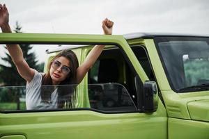 jolie femme dans la voiture moderne verte posant pour la caméra photo