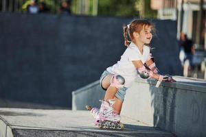 jolie petite fille avec des patins à roulettes à l'extérieur est assise sur la rampe pour les sports extrêmes photo