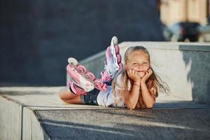 jolie petite fille avec des patins à roulettes à l'extérieur est assise sur la rampe pour les sports extrêmes photo