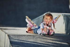 jolie petite fille avec des patins à roulettes à l'extérieur est assise sur la rampe pour les sports extrêmes photo