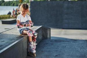 jolie petite fille avec des patins à roulettes à l'extérieur est assise sur la rampe pour les sports extrêmes photo