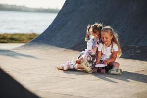 se détendre et discuter. sur la rampe pour les sports extrêmes. deux petites filles avec des patins à roulettes à l'extérieur s'amusent photo