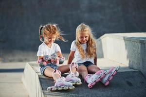 avoir du repos. sur la rampe pour les sports extrêmes. deux petites filles avec des patins à roulettes à l'extérieur s'amusent photo