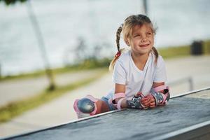 jolie petite fille avec des patins à roulettes à l'extérieur est assise sur la rampe pour les sports extrêmes photo