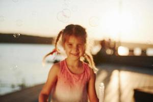 soleil incroyable. heureuse petite fille jouant avec des bulles près du lac au parc photo