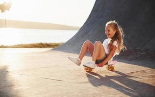 est assis sur le patin. journée ensoleillée. l'enfant s'amuse sur la rampe. joyeuse petite fille photo