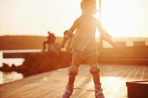 joyeux enfant mignon à cheval sur ses patins à roulettes. lumière du soleil incroyable photo