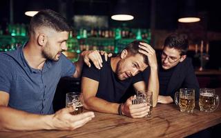 trois amis masculins dans le bar. soutenir un ami triste. unité des personnes. avec de la bière sur la table photo