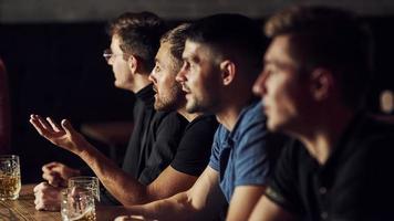 trois fans de sport dans un bar regardent le football. avec de la bière dans les mains photo