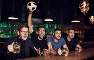 avec ballon de foot. c'est un objectif. célébrant la victoire. trois fans de sport dans un bar regardant le football avec de la bière dans les mains photo