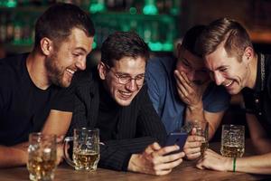 contenu amusant sur smartphone. trois amis se reposant dans le pub avec de la bière dans les mains. avoir une conversation photo