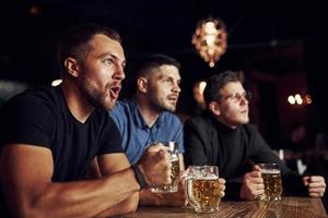 trois fans de sport dans un bar regardent le football. avec de la bière dans les mains photo