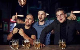 trois fans de sport dans un bar regardent le football. avec de la bière dans les mains photo