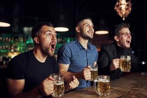 célébrant la victoire. trois fans de sport dans un bar regardent le football. avec de la bière dans les mains photo