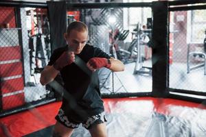 le jeune boxeur en bandages rouges fait de l'exercice. dans le gymnase sur la cage photo