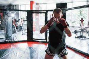 prêt à combattre. le jeune boxeur en bandages rouges fait de l'exercice. dans le gymnase sur la cage photo